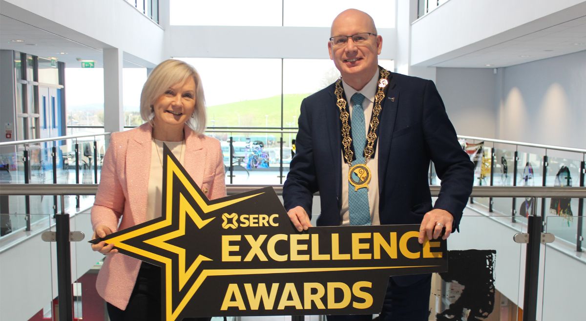 Woman with blond hair wearing pale pink jacket pictured with man in dark suit wearing chain of office.  Both holding cut out star shaped prop with words: SERC Excellence Awards